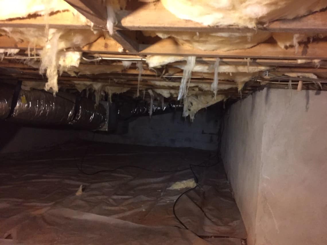 A failing vented crawl space in North Carolina: fiberglass batts sagging out of the floor joists above a bare dirt floor
